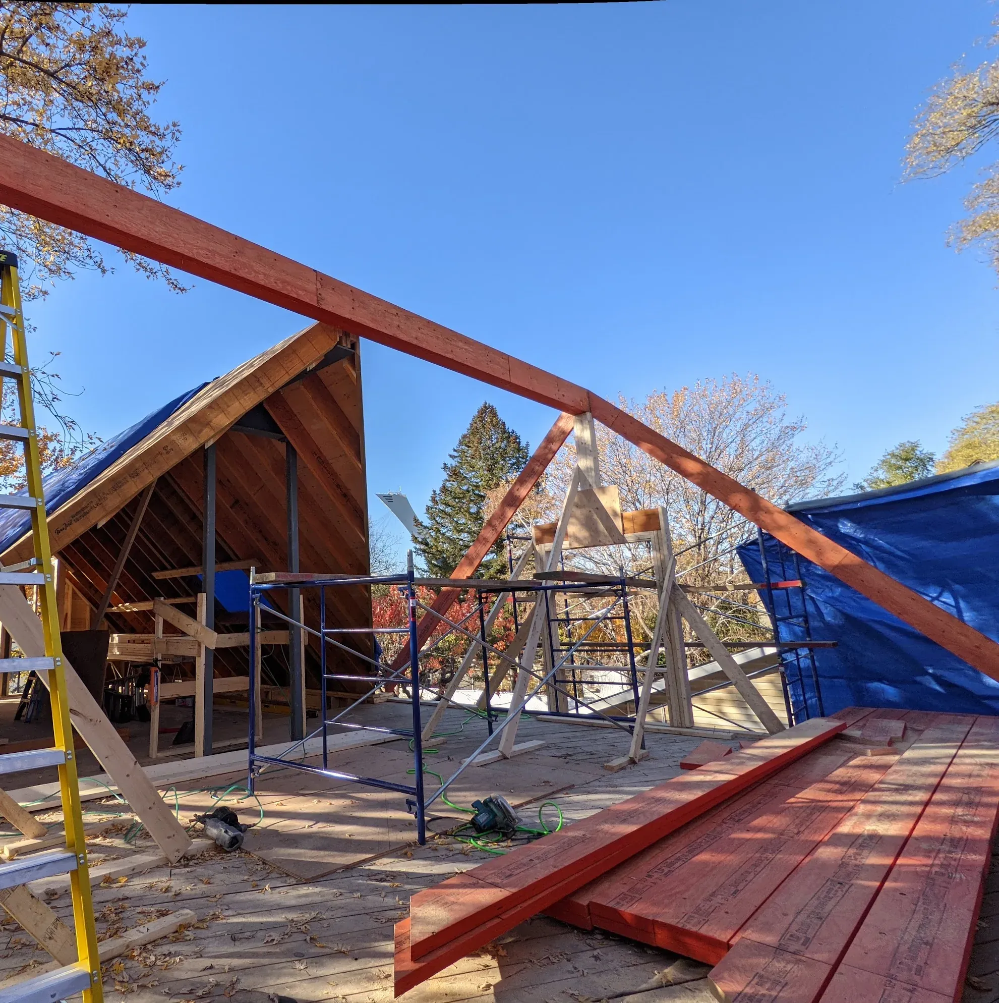 Long chevron d'ingénierie en bois lamellé posé en pente sur un appui temporaire, devant l'ossature d'un comble en cours de montage, d'autres chevrons empilés sur le plancher