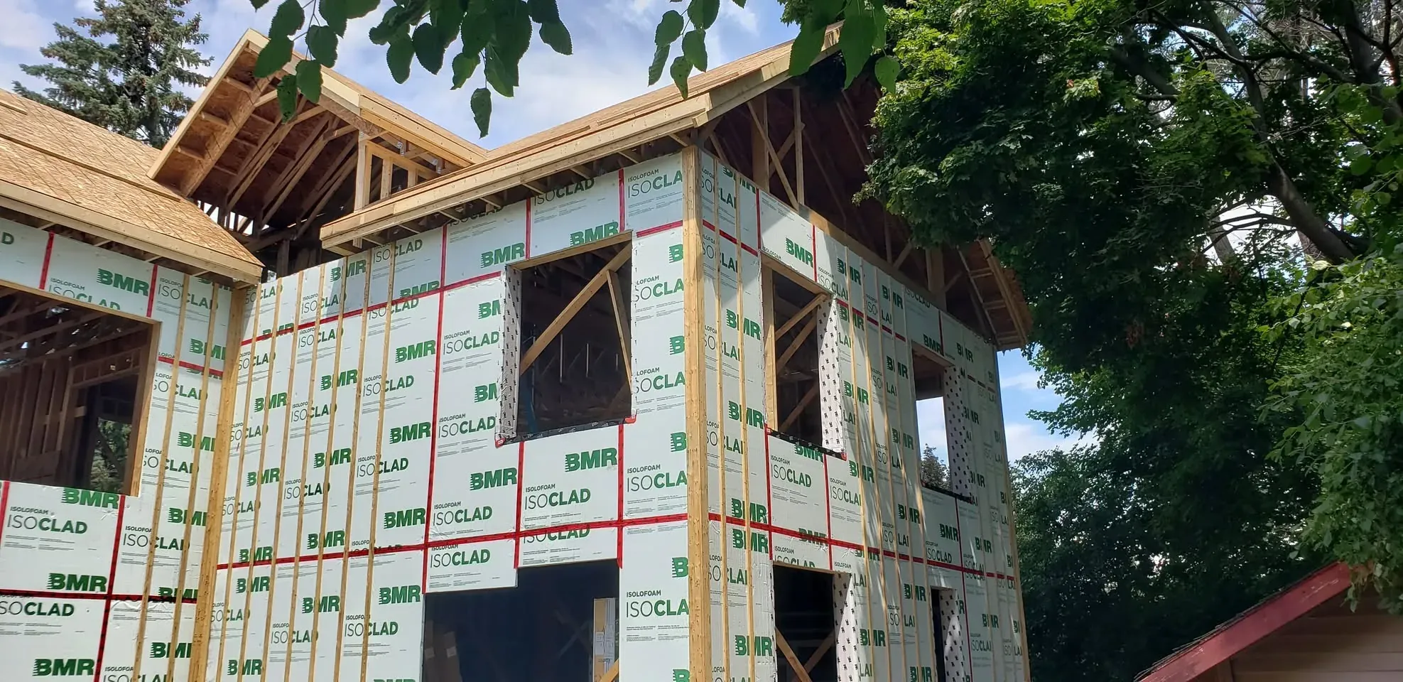 Maison neuve fermée en panneaux isolants, lucarne et débords de toit charpentés, vue en contre-plongée