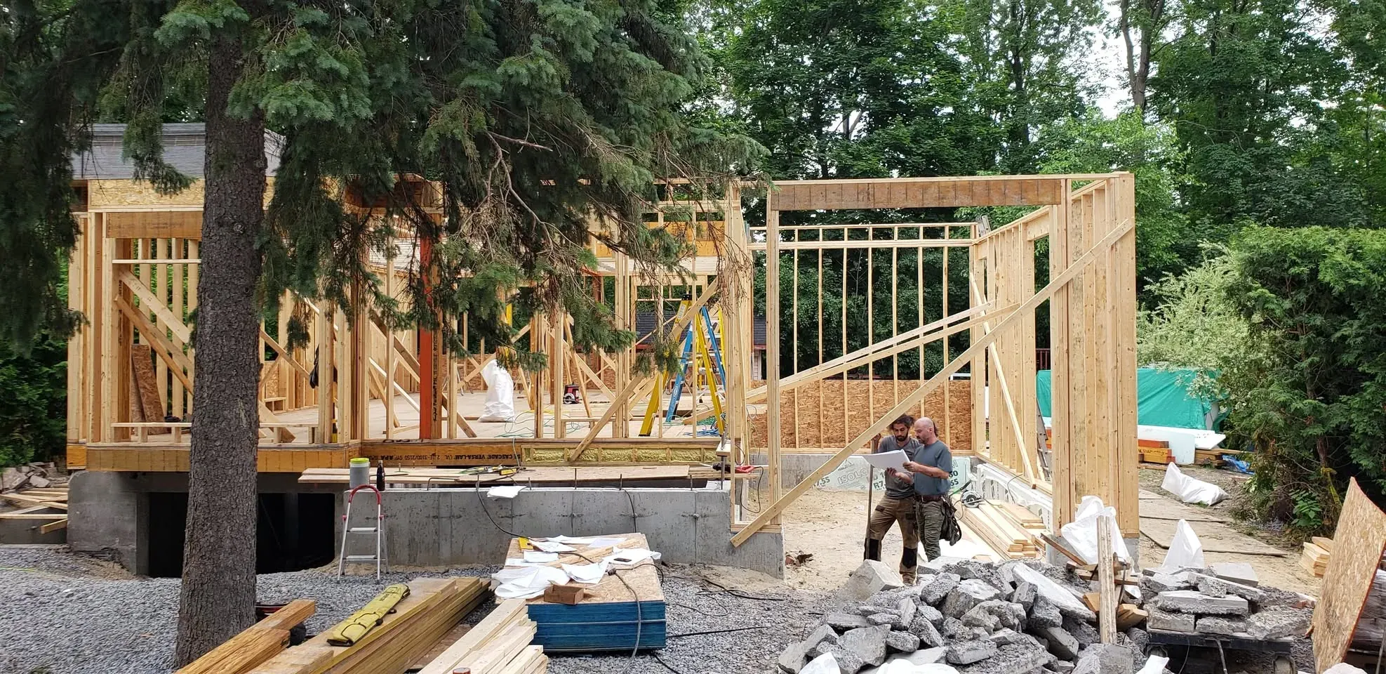 Deux charpentiers consultent un plan devant l'ossature de bois d'une maison neuve en construction