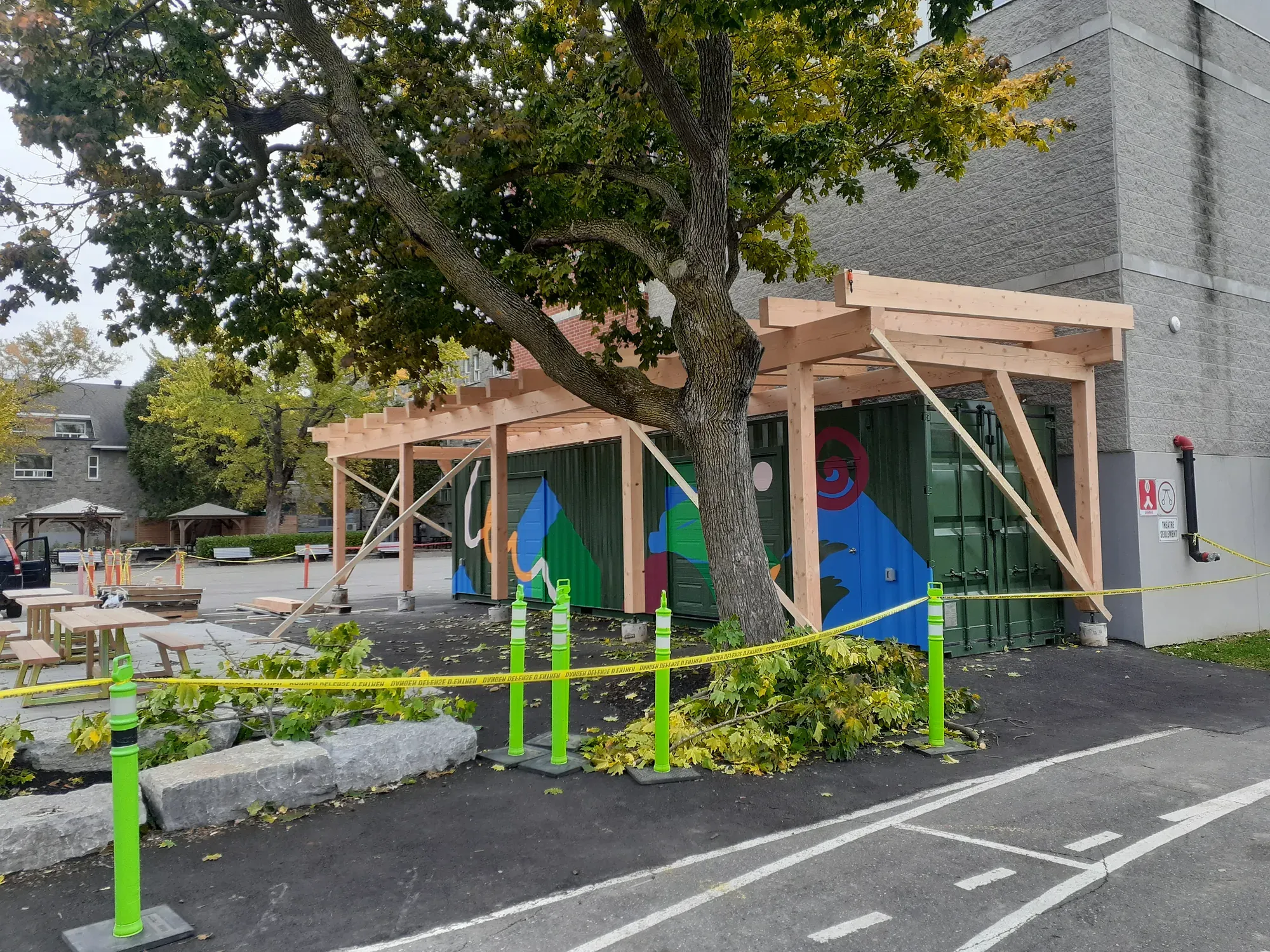 Auvent de bois neuf monté contre un bâtiment public, poteaux, aisseliers et poutres apparents, dans une cour aménagée