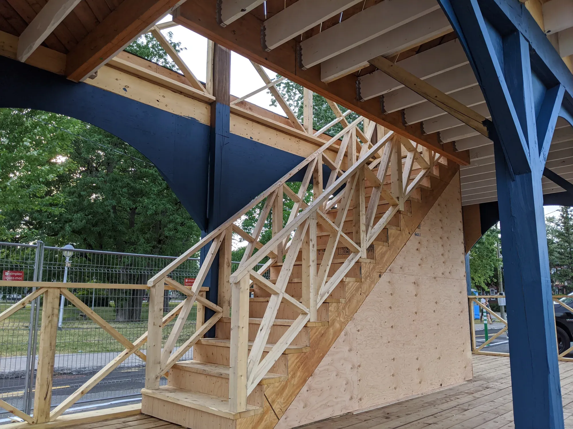Escalier de bois neuf menant à l'étage d'une halle publique, ossature et garde-corps en place sous la galerie