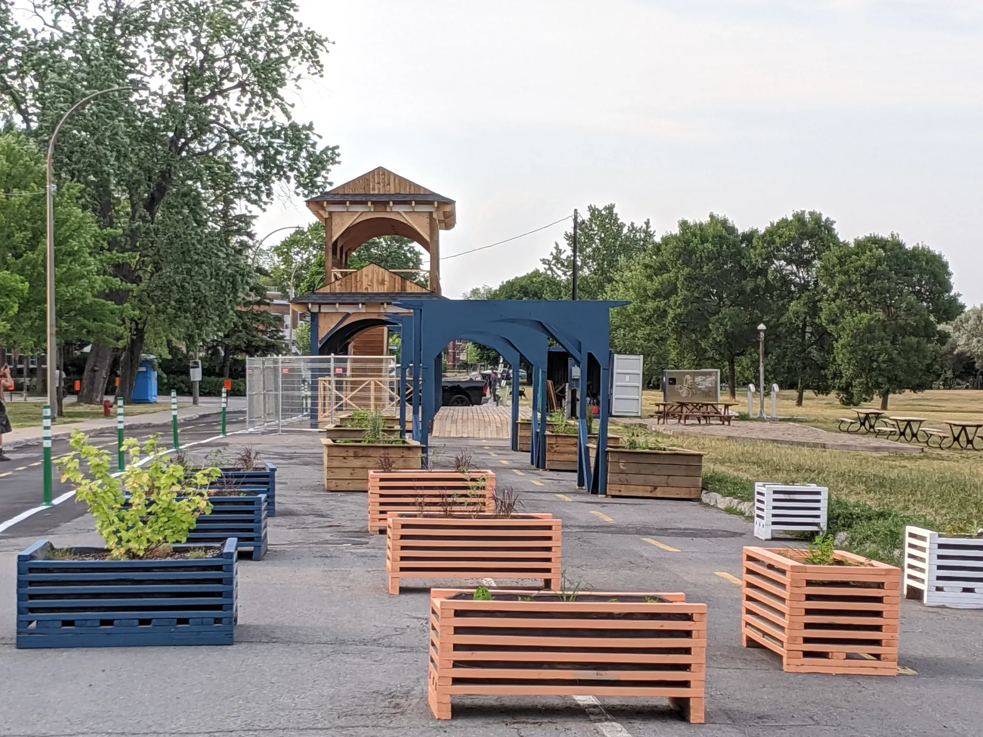 Place publique aménagée avec une halle de bois et un belvédère à deux étages, bacs de plantation devant