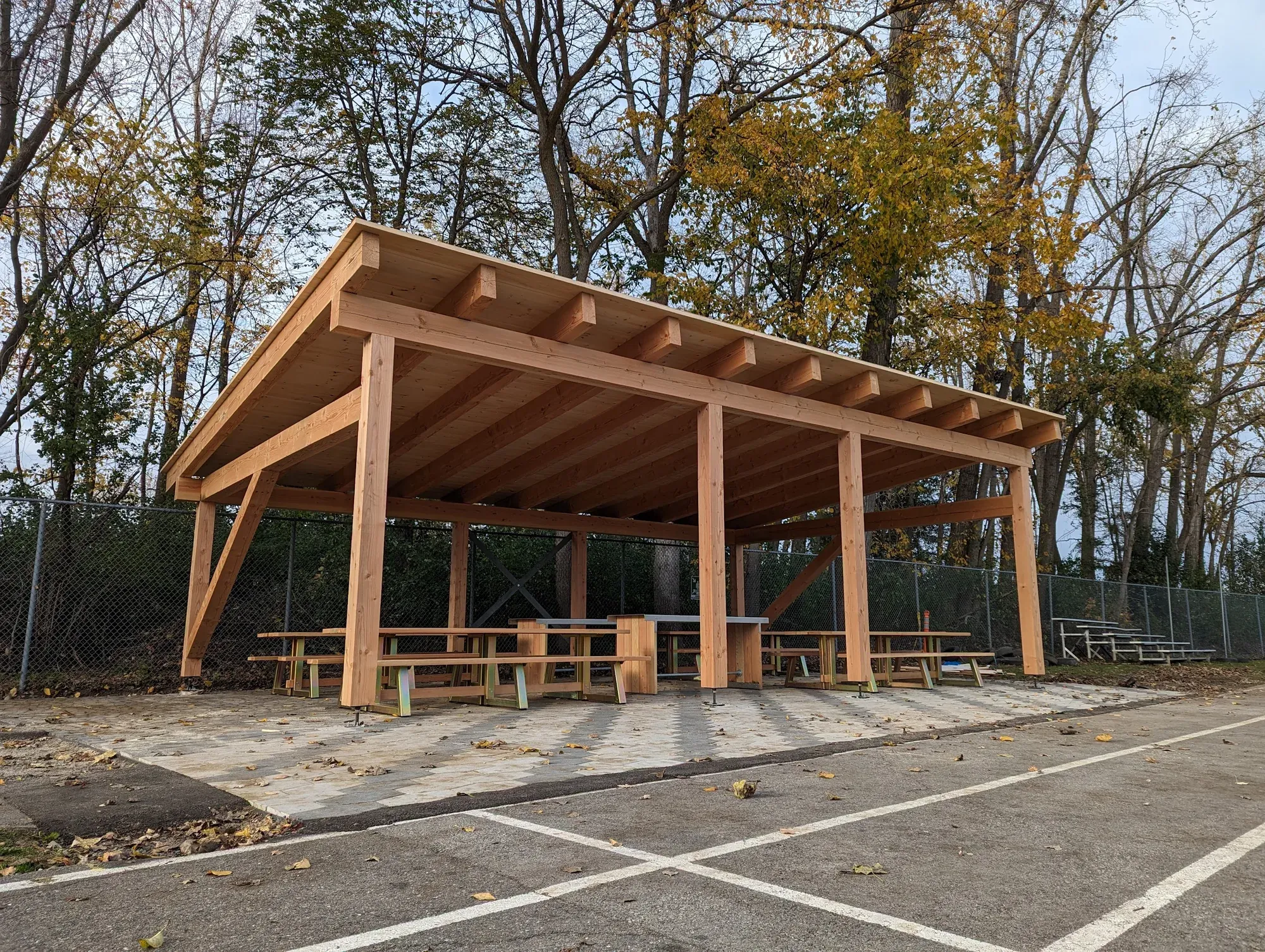 Préau de bois à toit plat vu de trois quarts, poutres et chevrons apparents, tables de pique-nique dessous