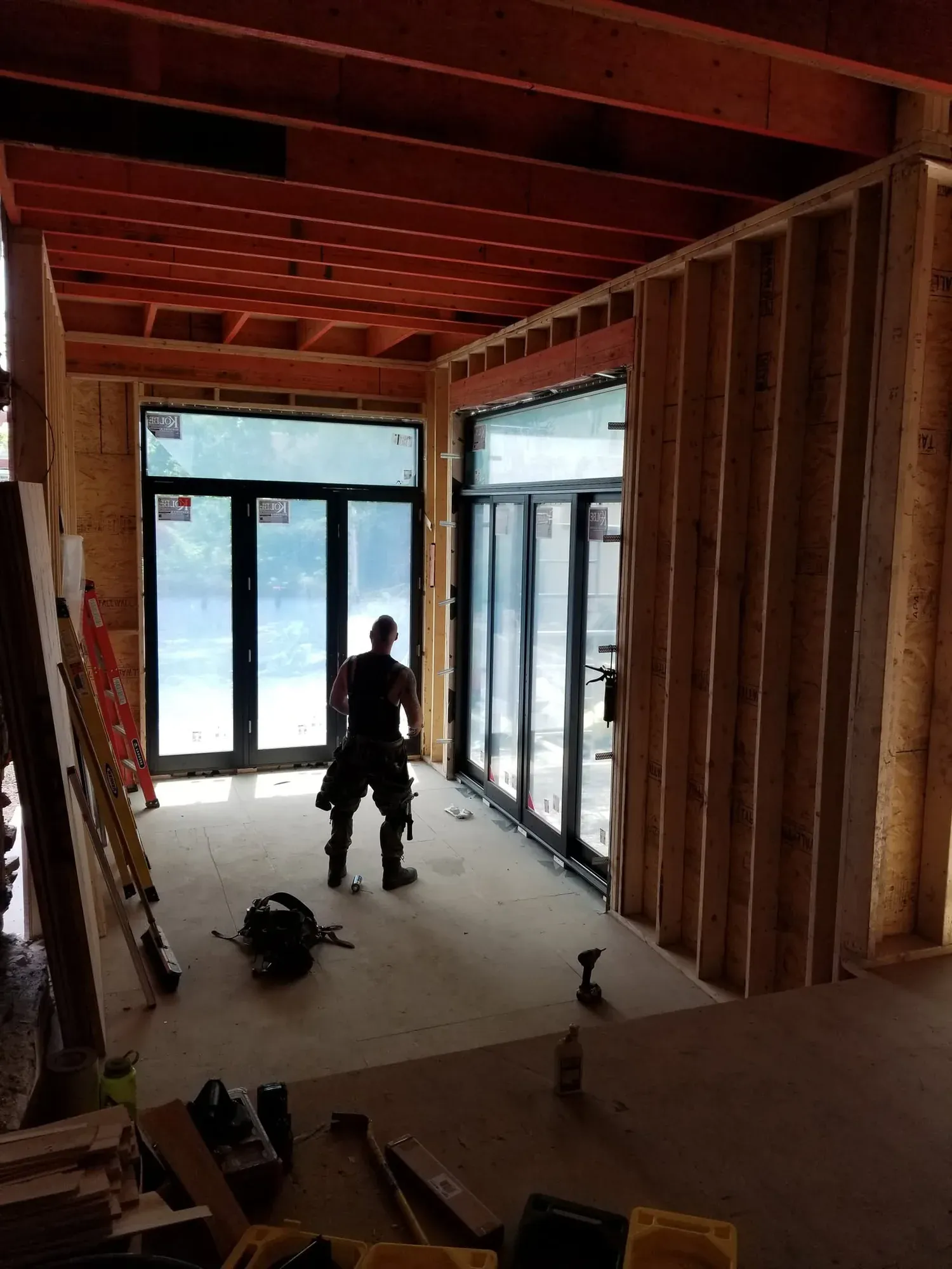 Grandes baies vitrées neuves posées dans l'ossature de bois d'une maison en rénovation, à contre-jour
