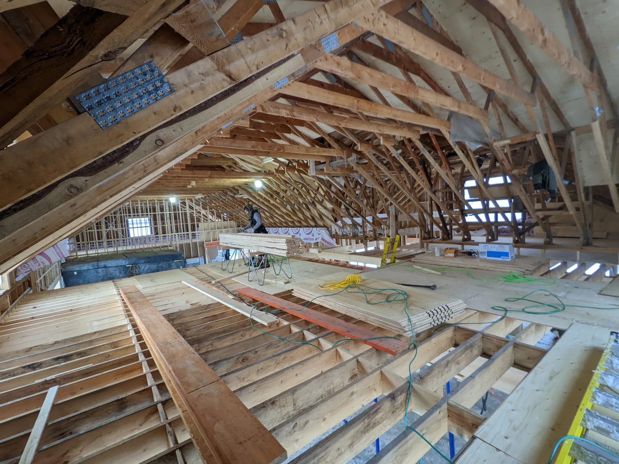 Grand comble d'une grange ancienne restaurée : fermes d'origine modifiées et reprises en bois neuf, plancher refait sur ses solives, poutres équarries noircies conservées