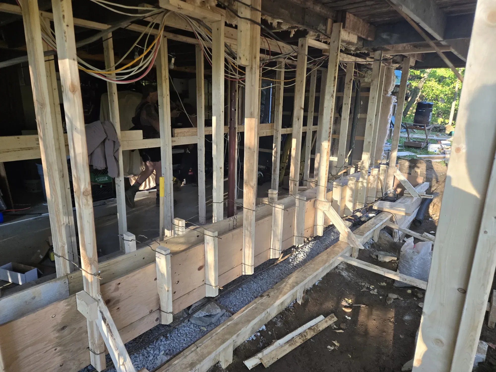 Maison soutenue par des poteaux de bois temporaires pendant qu'une semelle de béton neuve est coffrée sous le mur porteur