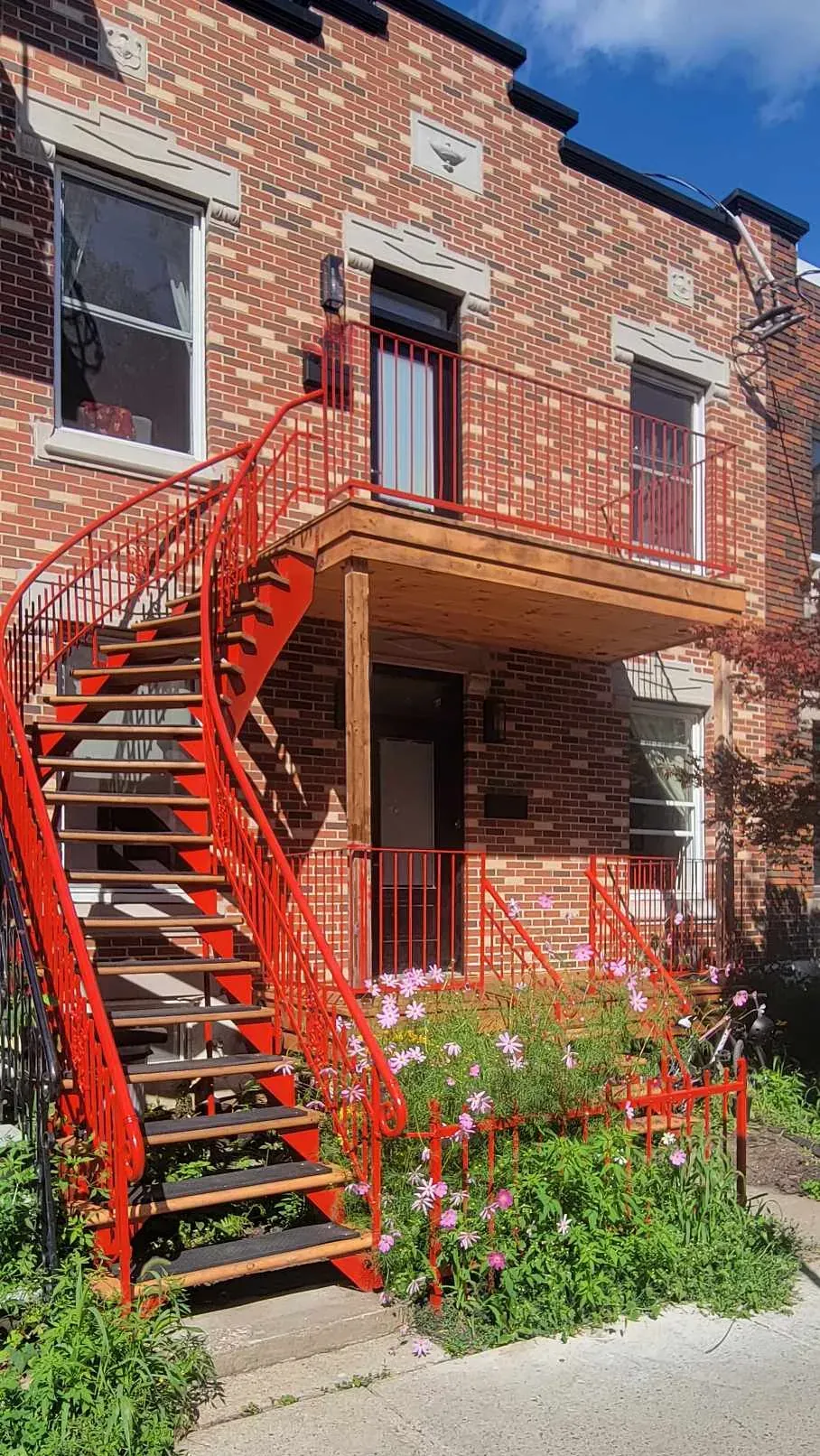 Galerie avant refaite en bois, avec son escalier extérieur tournant en métal rouge et son plancher neuf