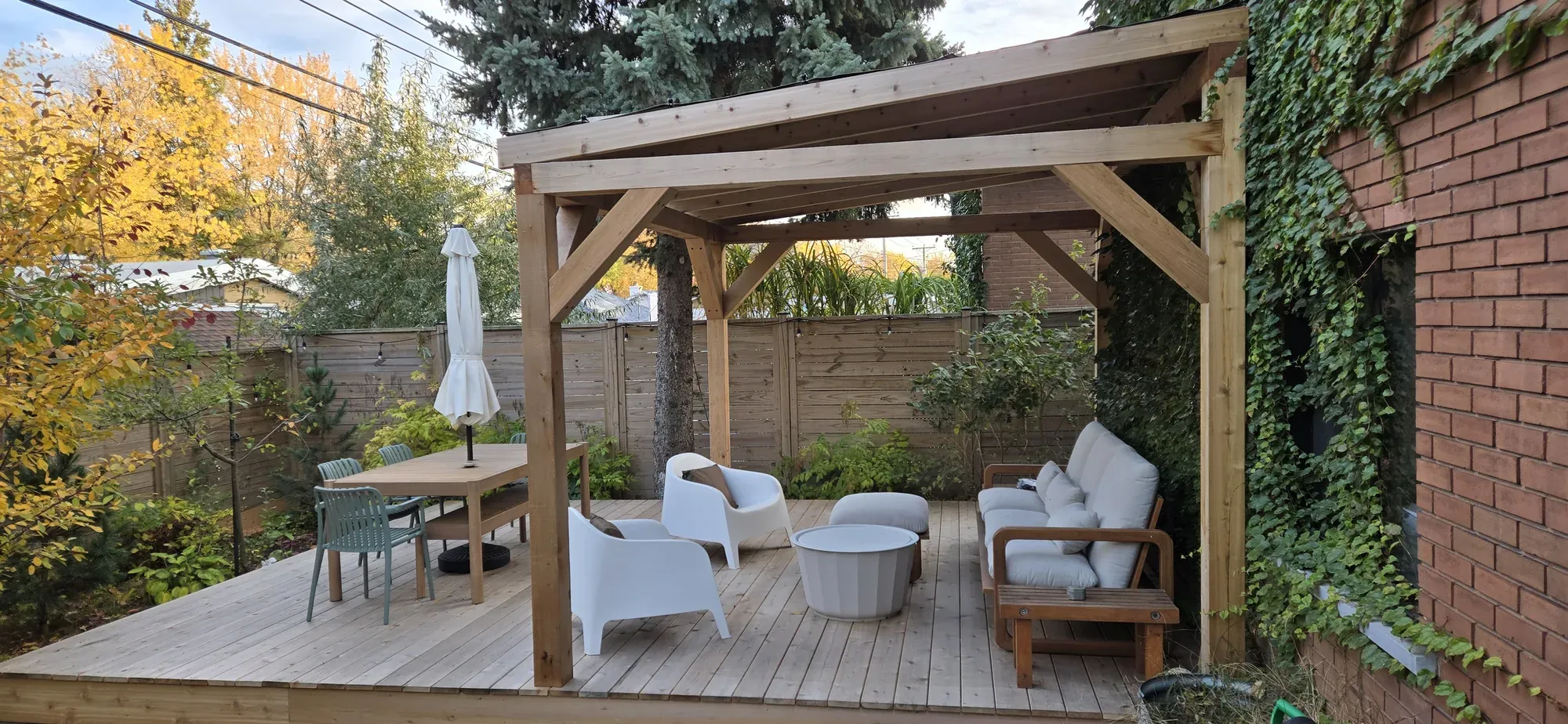 Pavillon de cèdre à toit simple pente monté sur une terrasse de bois, avec mobilier de jardin dessous