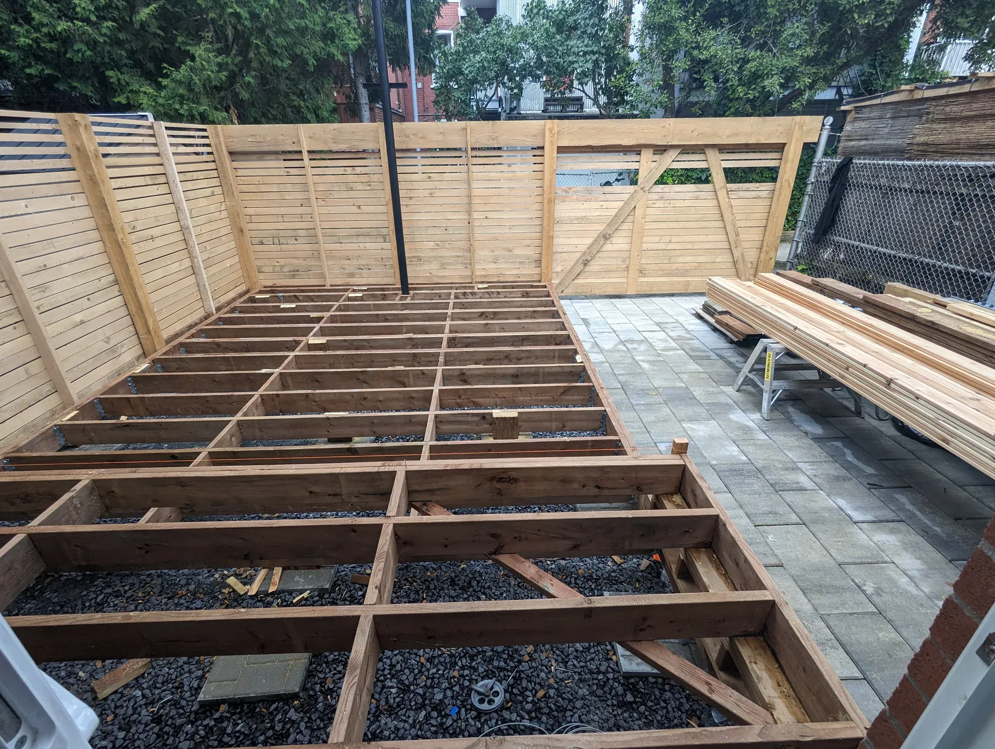 Structure de terrasse en construction : solivage de bois traité posé sur pierre concassée, entouré d'écrans à claire-voie